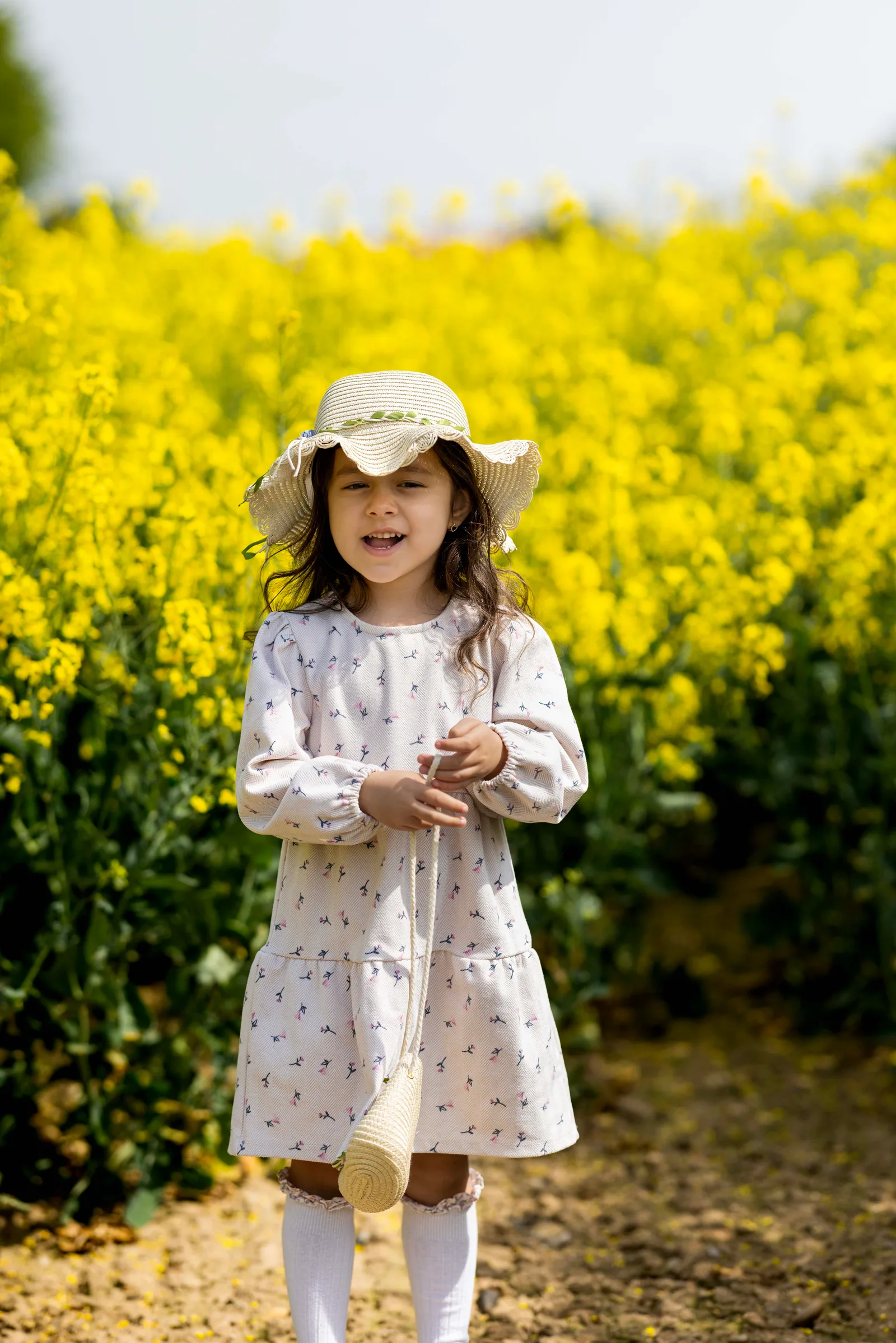 Little girl in a straw hat walking through a yellow flower field