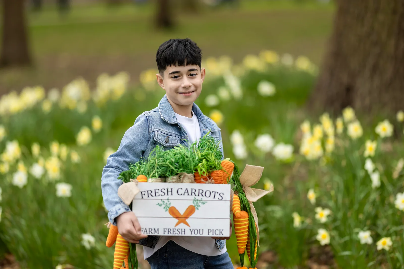 Teen boy holding a wooden crate of fresh carrots in a flower field