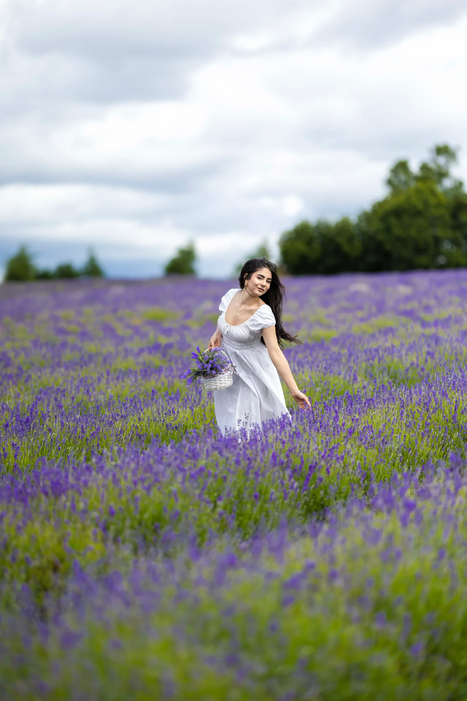 Woman in white dress walking through lavender field holding a bouquet