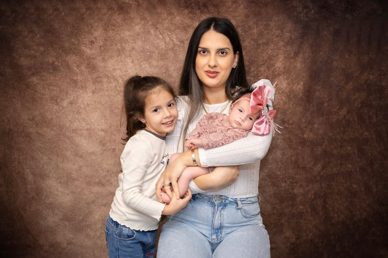 Mother with her two daughters, one older and a newborn, captured in warm studio tones.