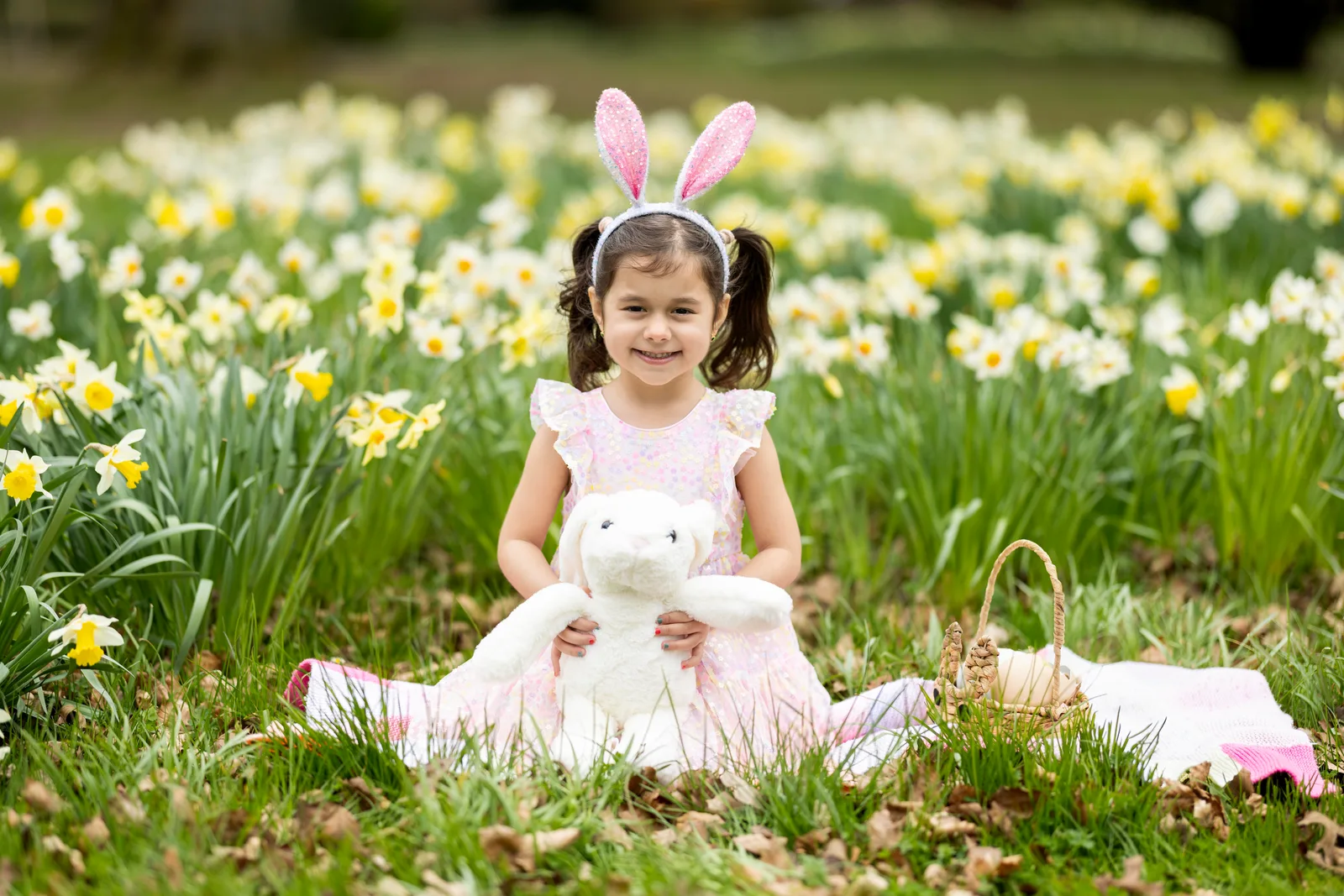 Little girl with bunny ears holding a white teddy bear in a daffodil field