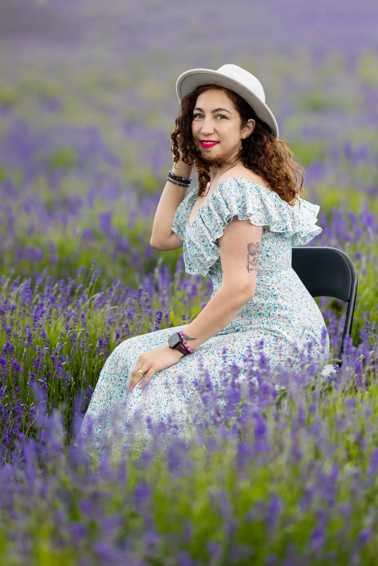 Woman in floral dress and sunhat seated among lavender rows
