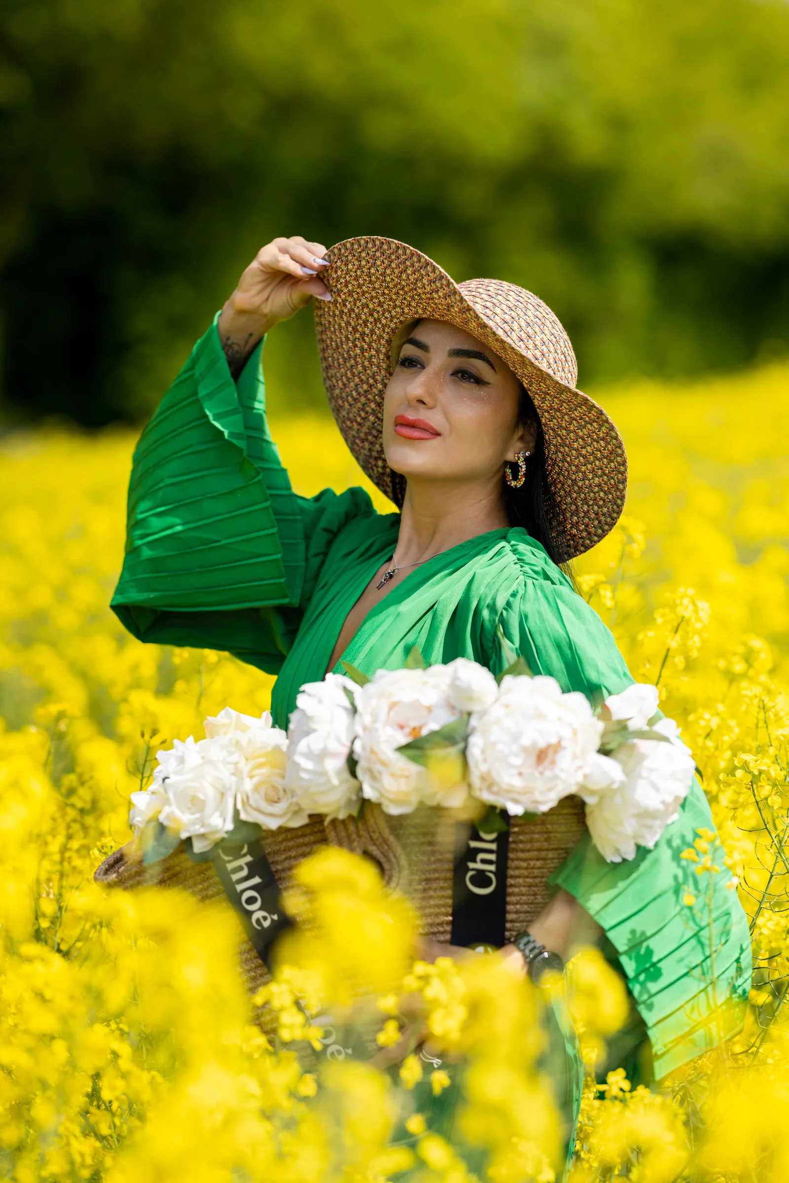 Woman in green dress adjusting straw hat among yellow flowers