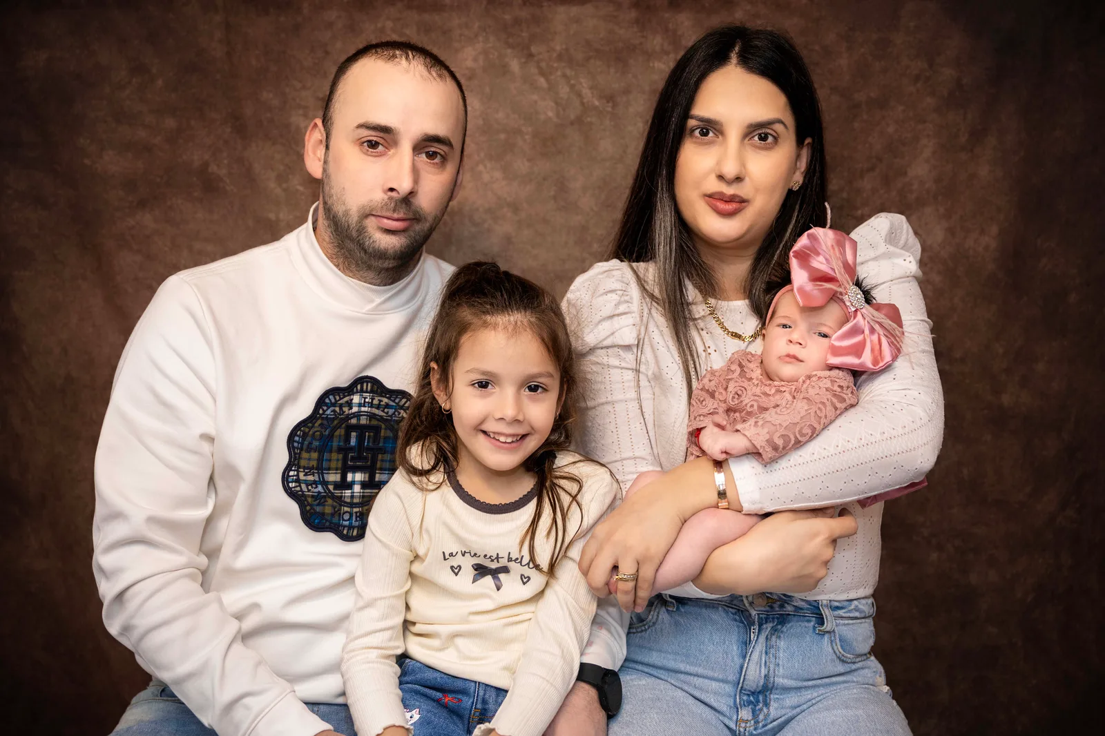 Family of four — parents and their two daughters — in a warm studio portrait.