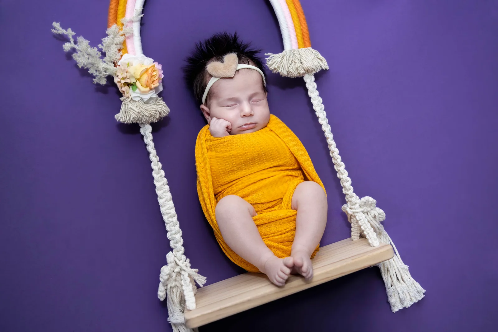 Newborn resting sweetly on a wooden swing, framed by soft macramé details.