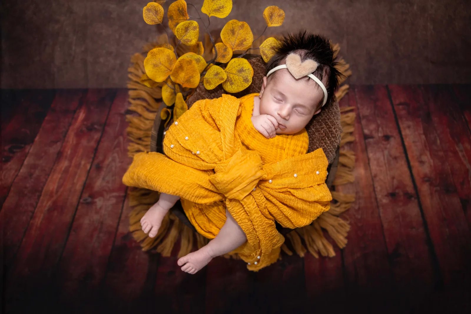 Newborn wrapped in a mustard knit, nestled among warm golden blooms.