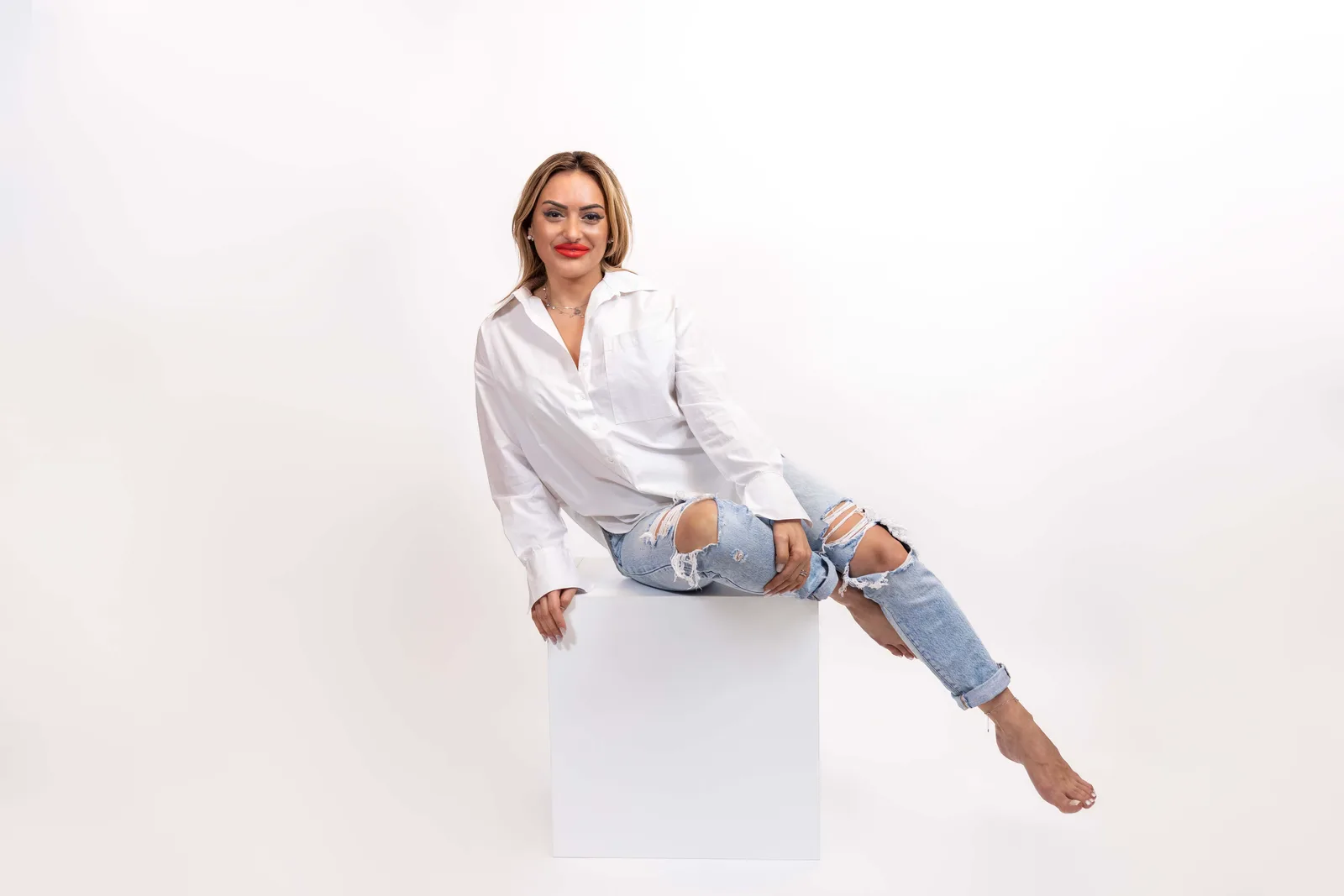 Casual studio portrait featuring a white top and jeans against a minimalist white backdrop.