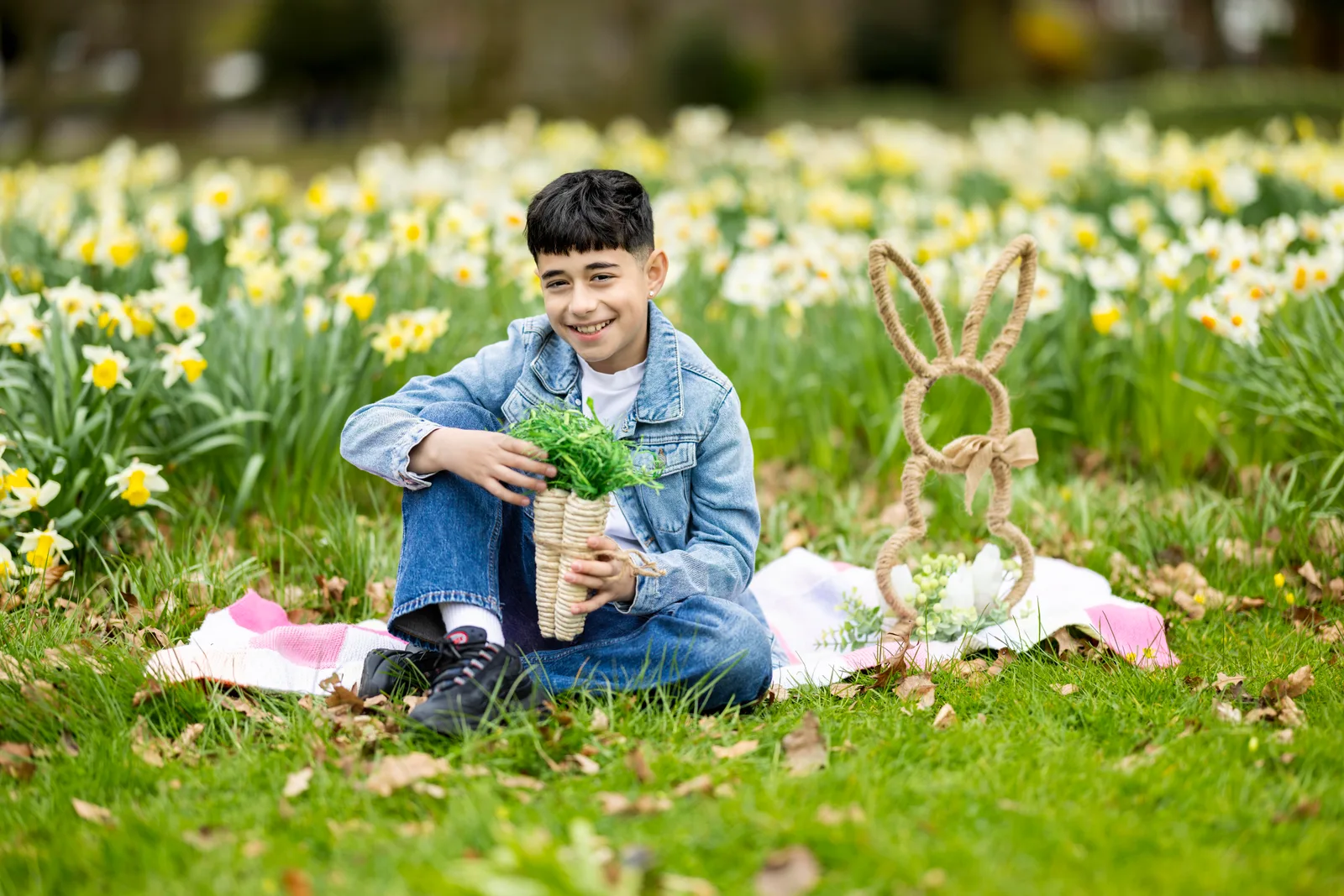 Teen boy smiling in a denim jacket holding a basket of greens in a flower field
