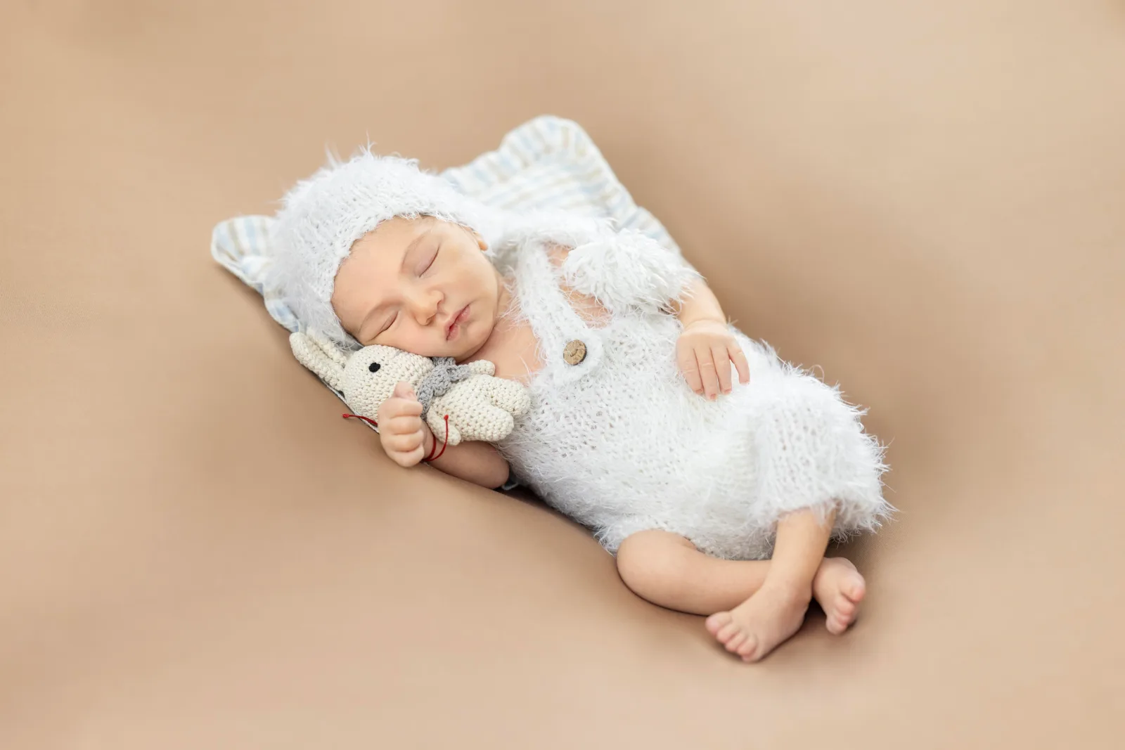 Sleeping newborn in a white knitted outfit holding a crochet bunny toy