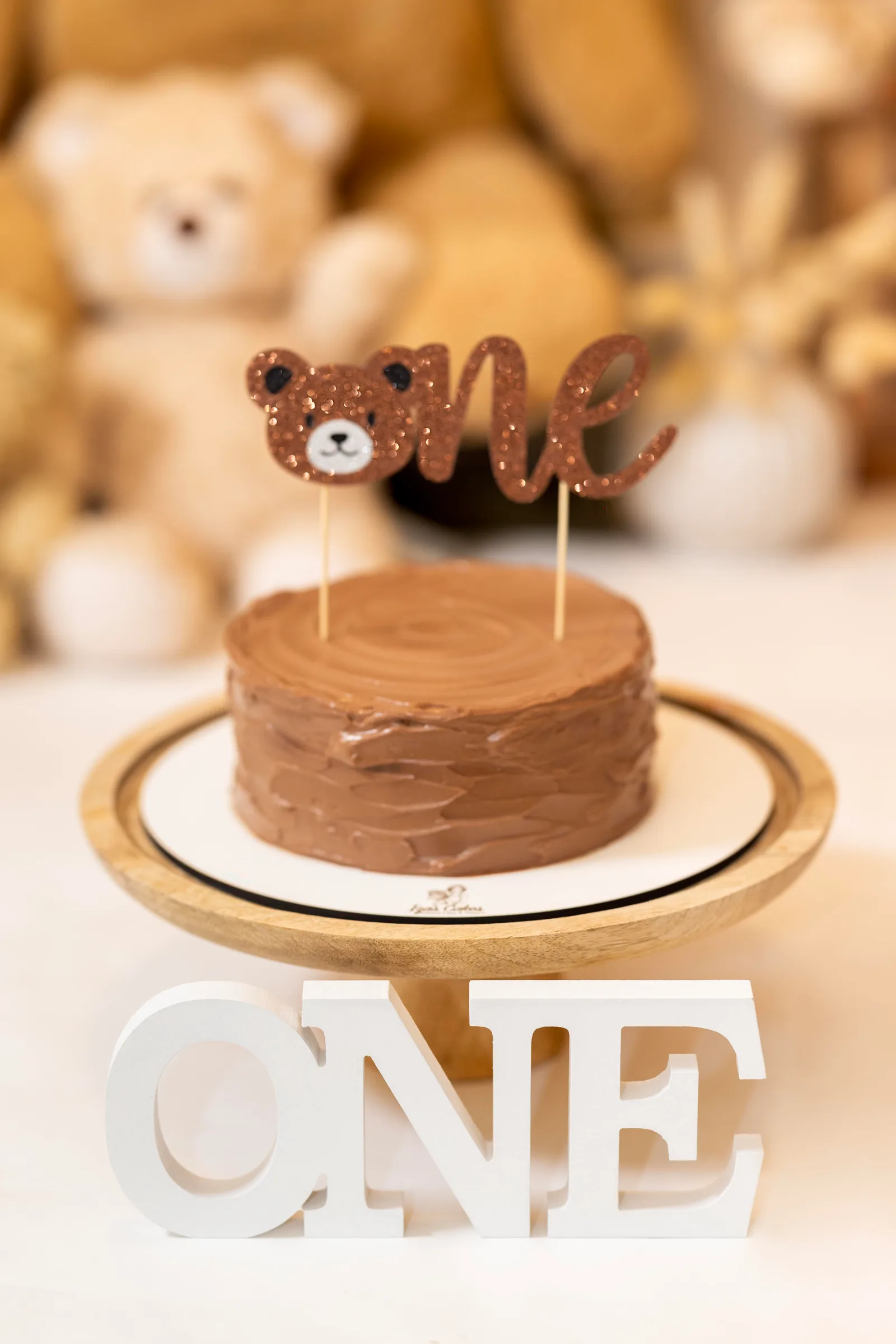 Chocolate smash cake with a bear-shaped 'one' topper beside wooden ONE letters
