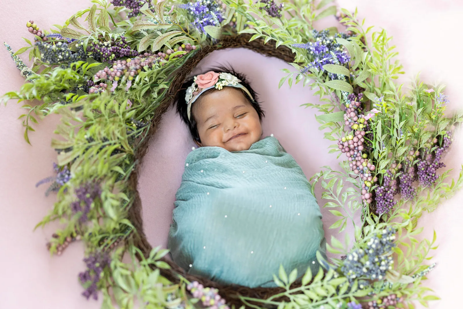 Sleeping baby in a teal wrap nestled in a flower and vine nest with lavender blooms