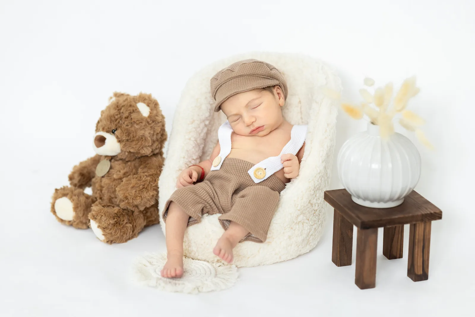 Newborn asleep in a fuzzy basket dressed as a little gentleman with cap and suspenders