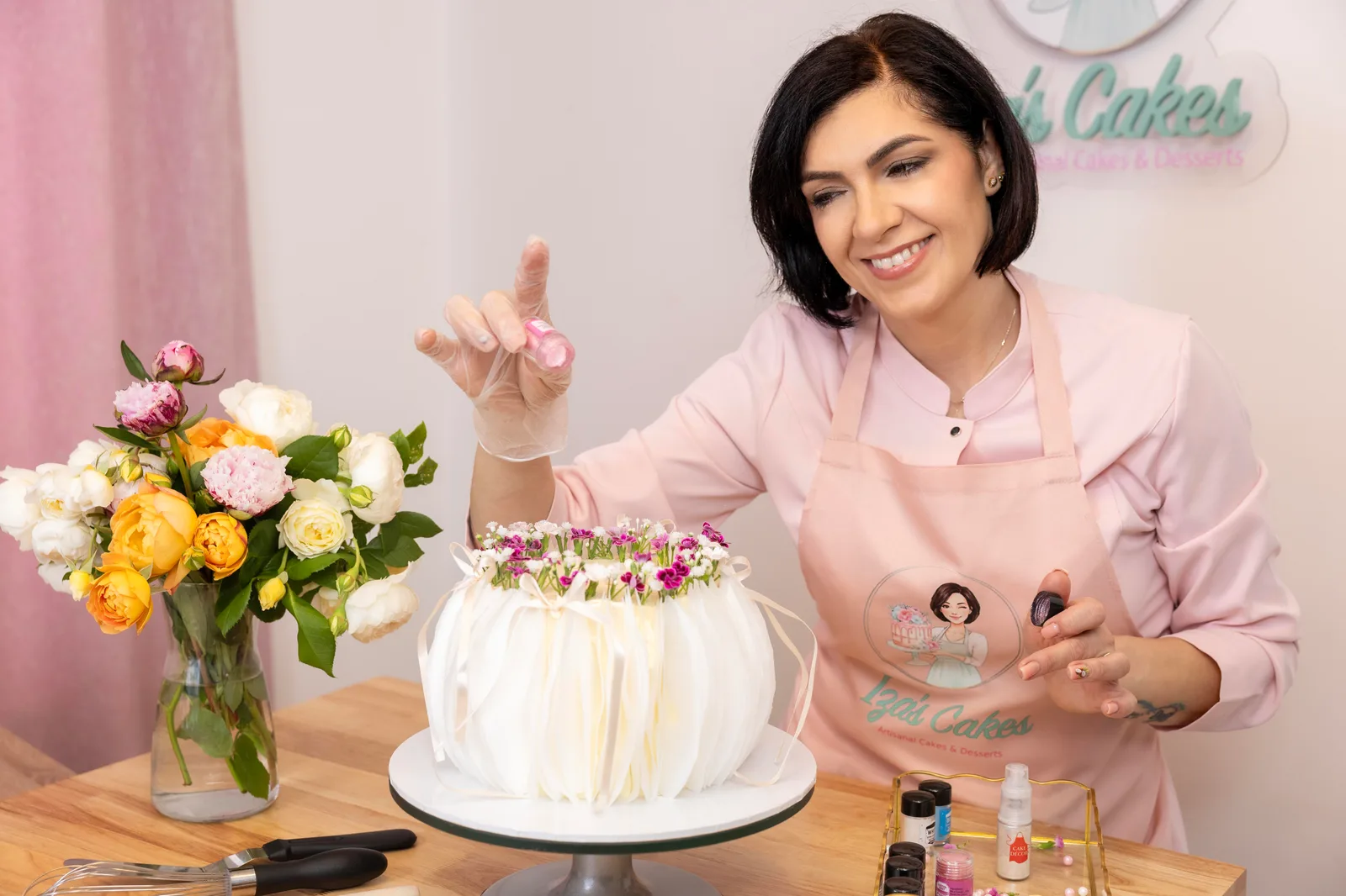Woman in a pink apron decorating a white cake with fresh flowers
