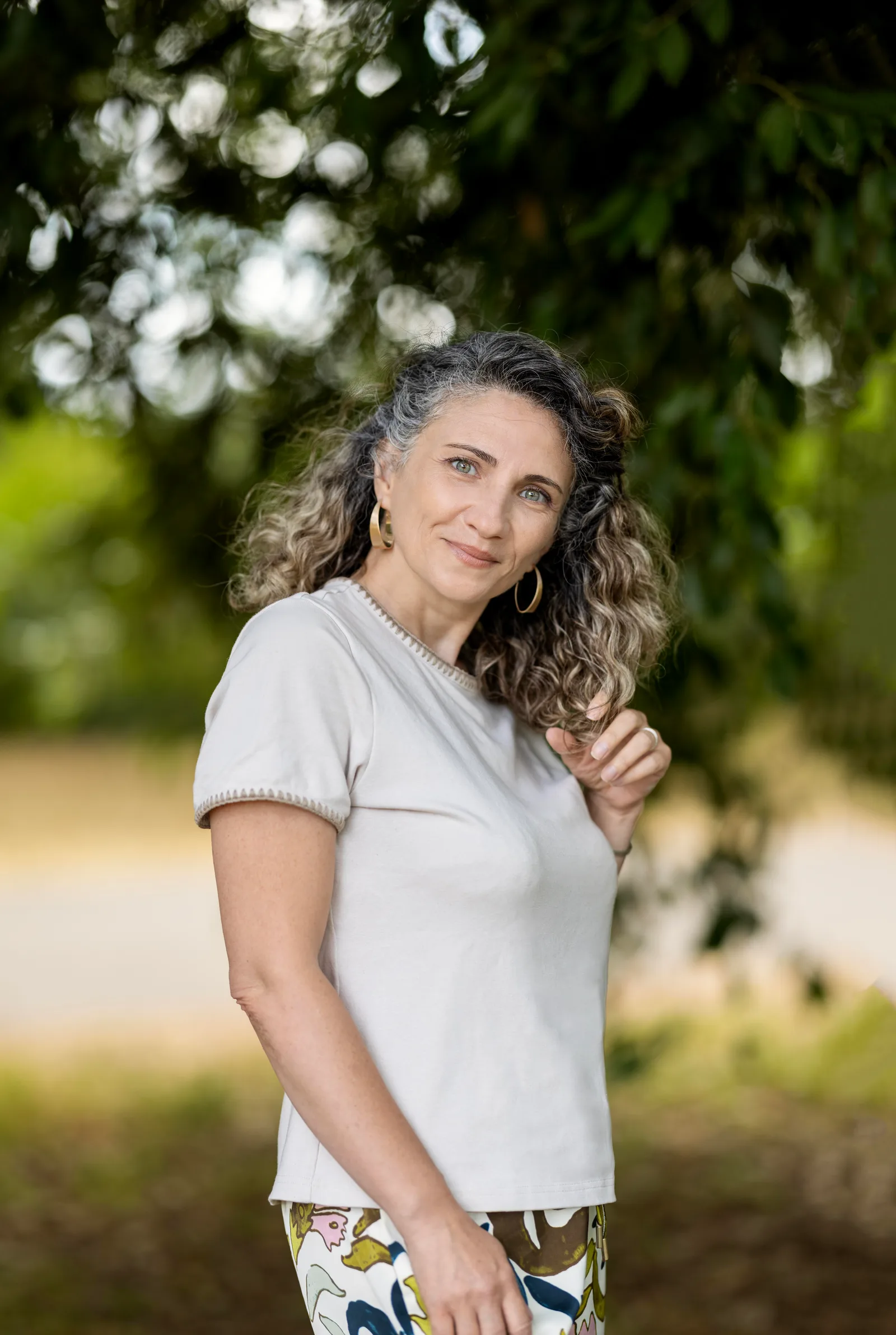 Woman with curly hair in a white t-shirt smiling outdoors in a green park