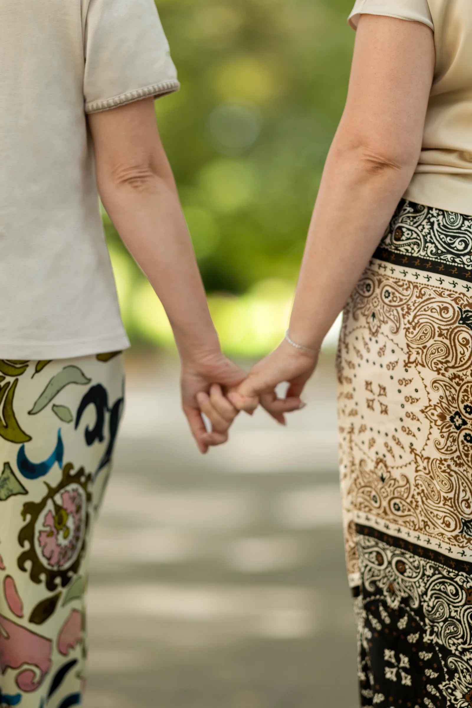 Close-up of two women holding hands while walking together in matching patterned trousers