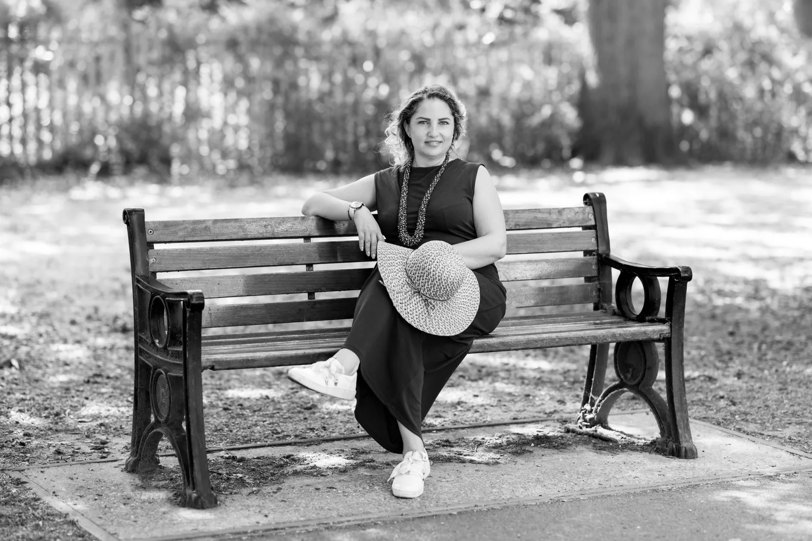 Black and white portrait of a woman sitting on a bench holding a sun hat