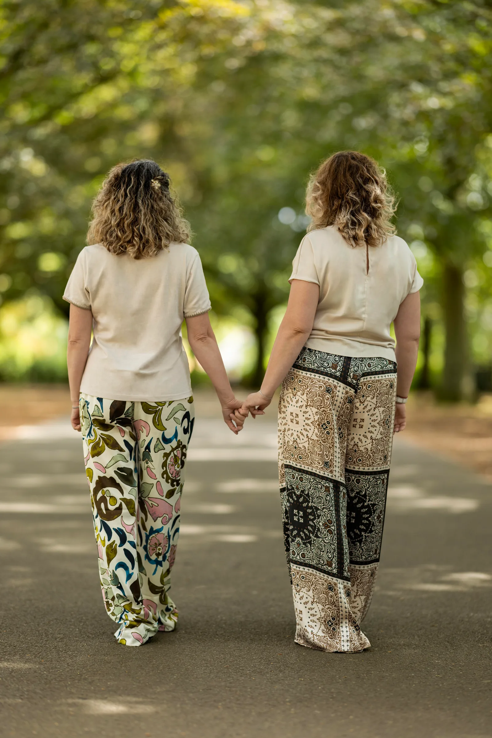 Two women walking hand in hand down a tree-lined path in matching outfits